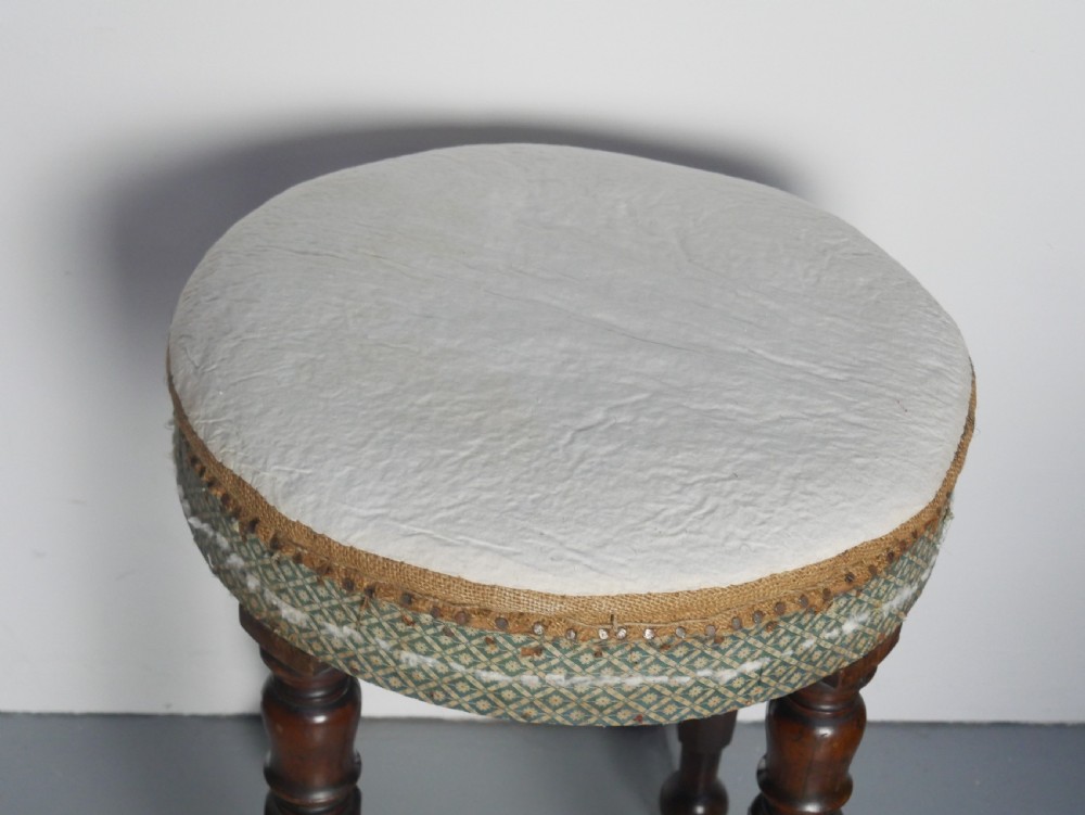 A circular stool with four dark turned timber legs and a padded circular top showing visible upholstery layers. View II