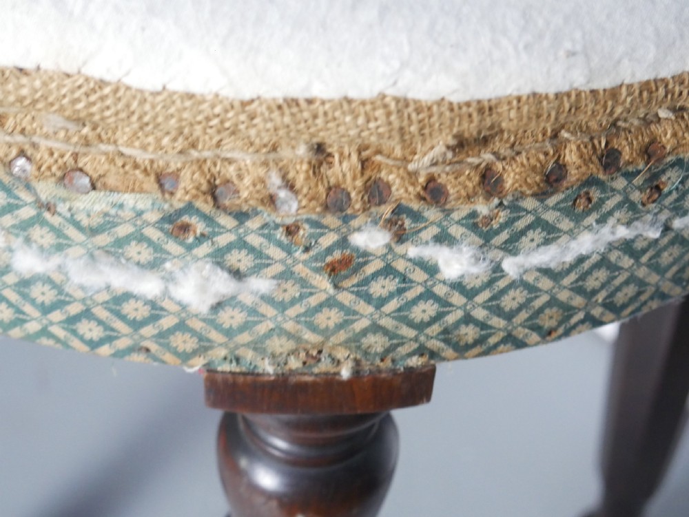 A circular stool with four dark turned timber legs and a padded circular top showing visible upholstery layers. View V