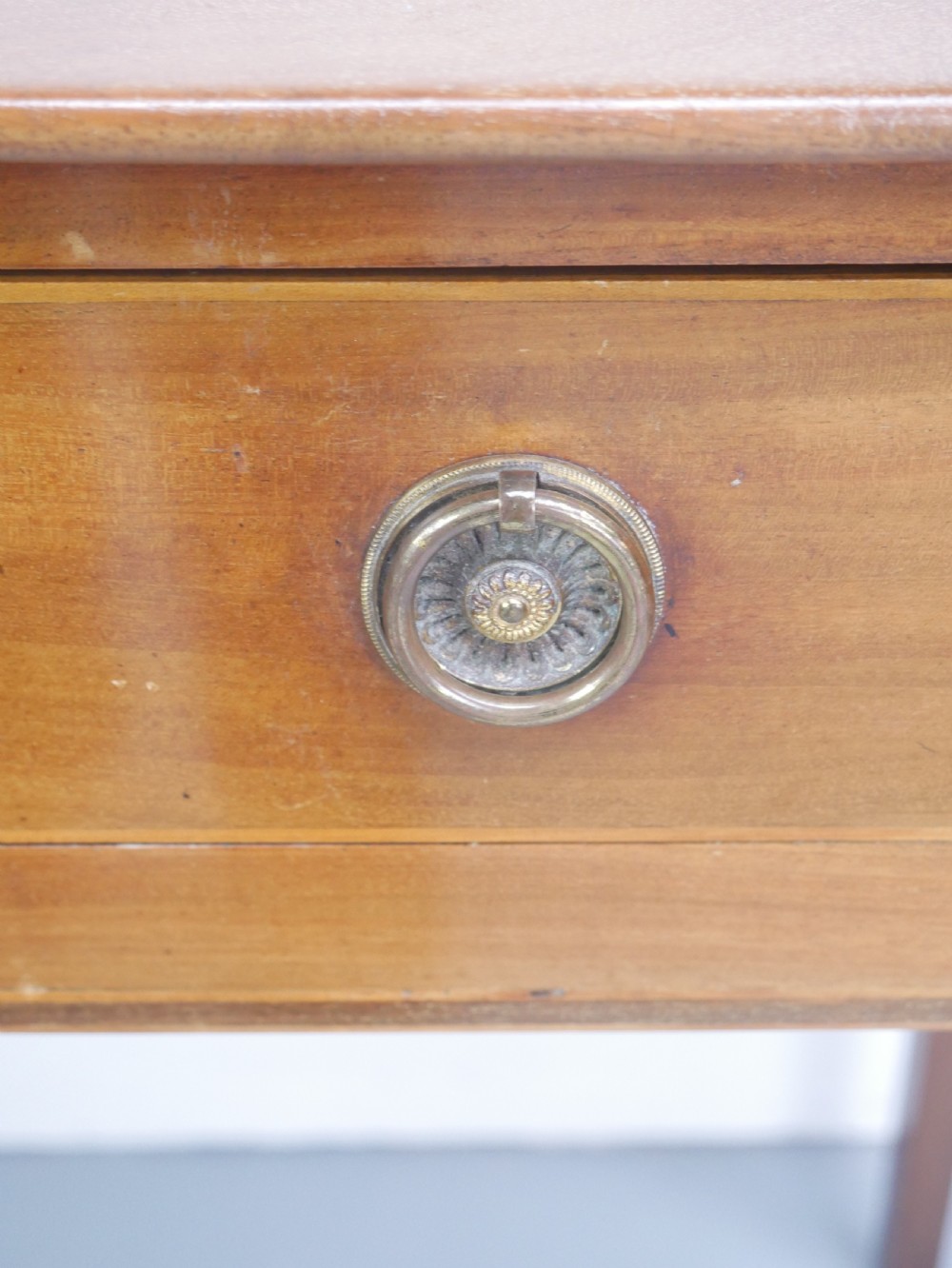 An antique mahogany writing table featuring a low gallery shelf, two drawers with circular brass pull handles, line inlay details, and four square tapered legs. View III