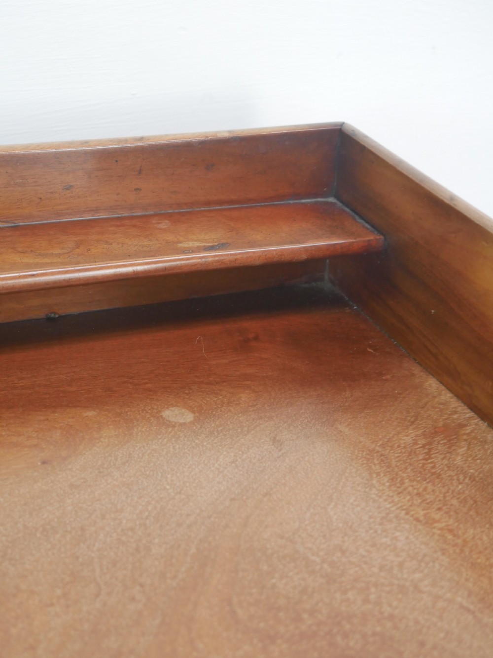 An antique mahogany writing table featuring a low gallery shelf, two drawers with circular brass pull handles, line inlay details, and four square tapered legs. View IV
