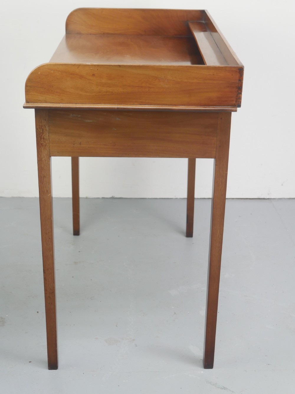 An antique mahogany writing table featuring a low gallery shelf, two drawers with circular brass pull handles, line inlay details, and four square tapered legs. View IX