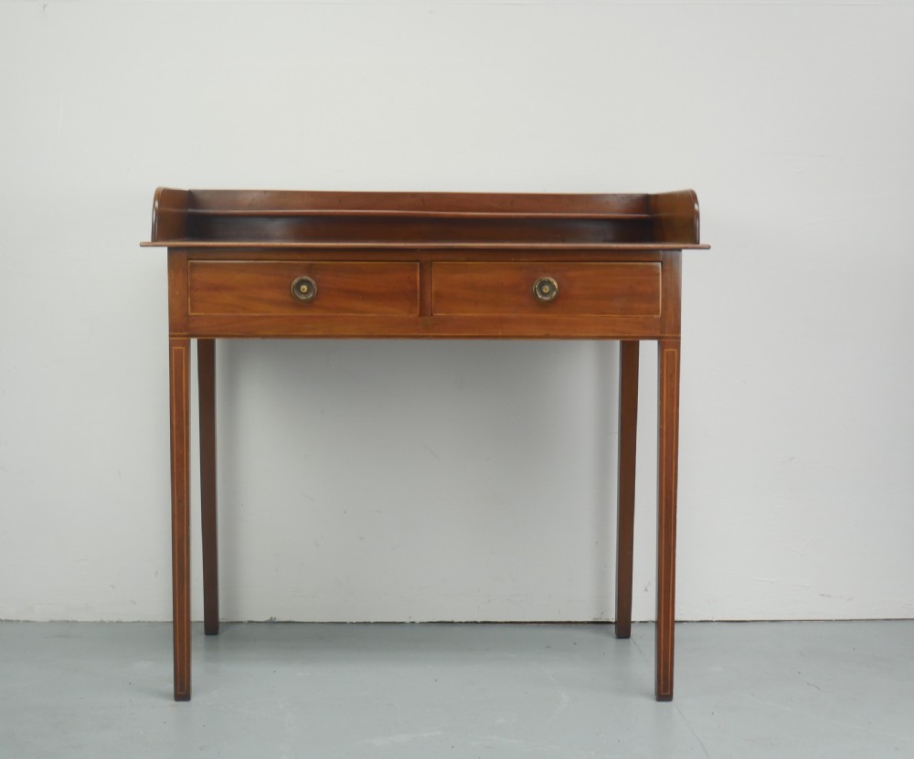 An antique mahogany writing table featuring a low gallery shelf, two drawers with circular brass pull handles, line inlay details, and four square tapered legs. View XI