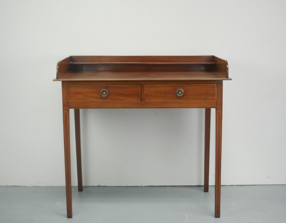 An antique mahogany writing table featuring a low gallery shelf, two drawers with circular brass pull handles, line inlay details, and four square tapered legs. View XII