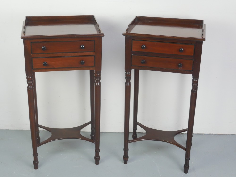 A pair of tall slim dark mahogany bedside tables featuring tray tops, two drawers with black knobs, turned legs, and curved X-frame stretchers.