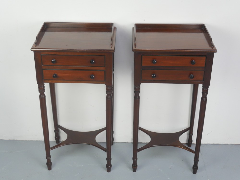 A pair of tall slim dark mahogany bedside tables featuring tray tops, two drawers with black knobs, turned legs, and curved X-frame stretchers. View V