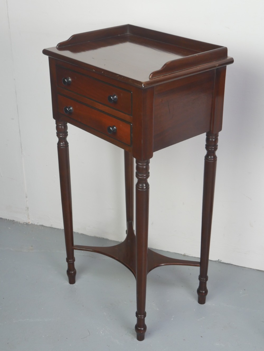 A pair of tall slim dark mahogany bedside tables featuring tray tops, two drawers with black knobs, turned legs, and curved X-frame stretchers. View VII