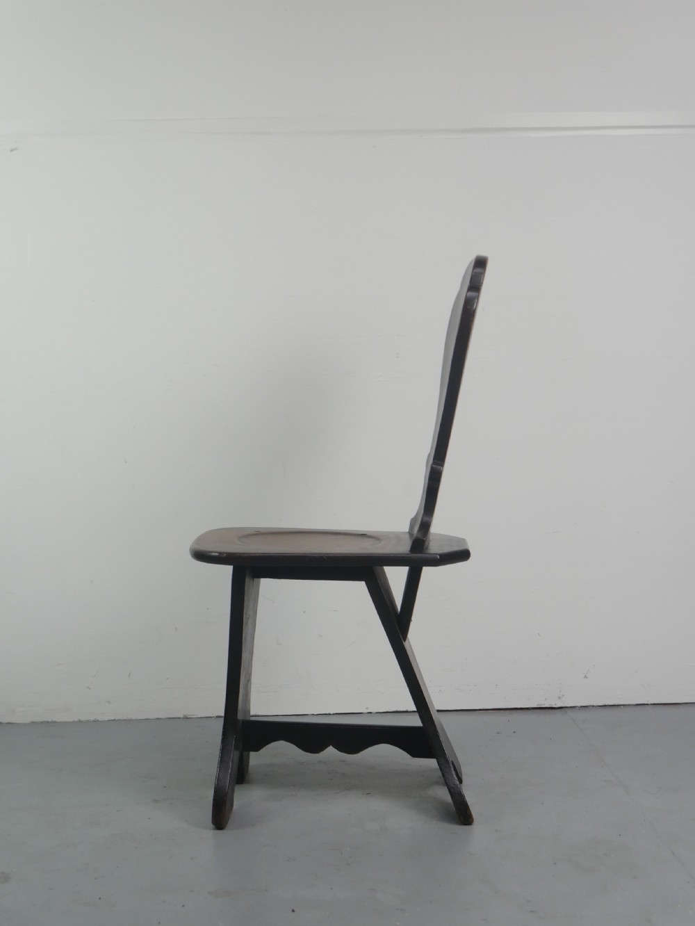 A pair of dark brown 18th-century oak sgabello hall chairs with shaped backrests and trestle bases set against a plain white background. View III