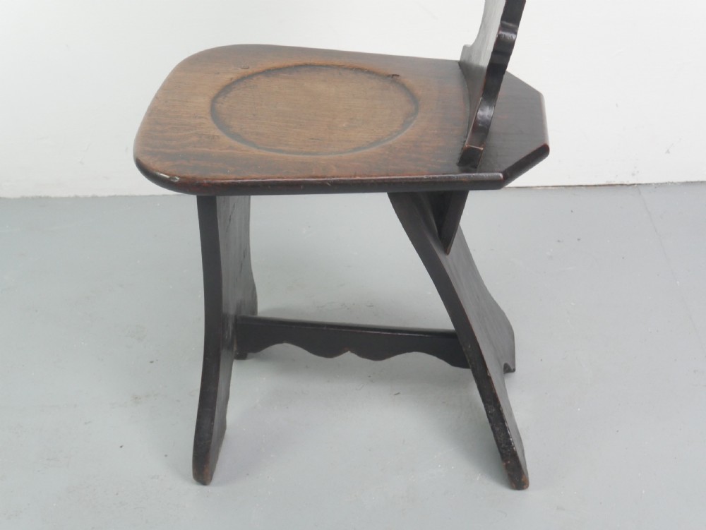 A pair of dark brown 18th-century oak sgabello hall chairs with shaped backrests and trestle bases set against a plain white background. View IV