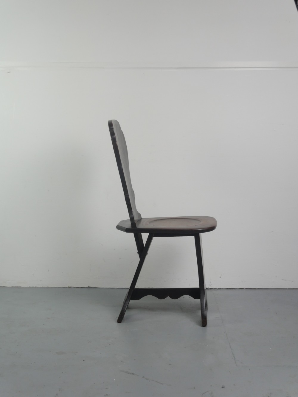 A pair of dark brown 18th-century oak sgabello hall chairs with shaped backrests and trestle bases set against a plain white background. View V