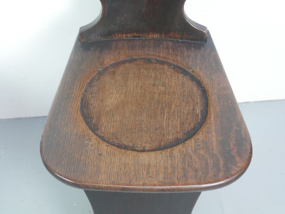 A pair of dark brown 18th-century oak sgabello hall chairs with shaped backrests and trestle bases set against a plain white background. View VI