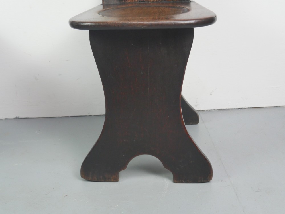 A pair of dark brown 18th-century oak sgabello hall chairs with shaped backrests and trestle bases set against a plain white background. View VII