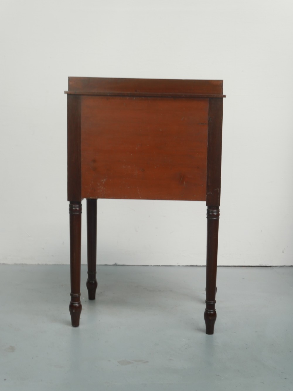 A Regency mahogany bedside cupboard featuring a reeded tambour door, fine boxwood stringing inlay, a raised tray top gallery, and slender turned legs. View VII