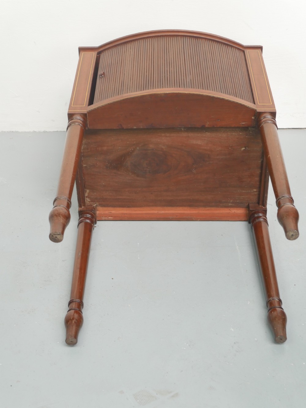A Regency mahogany bedside cupboard featuring a reeded tambour door, fine boxwood stringing inlay, a raised tray top gallery, and slender turned legs. View IX