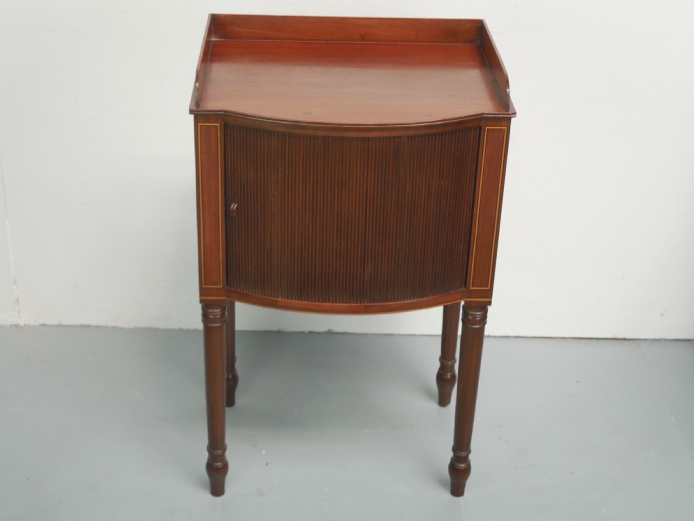 A Regency mahogany bedside cupboard featuring a reeded tambour door, fine boxwood stringing inlay, a raised tray top gallery, and slender turned legs. View XI