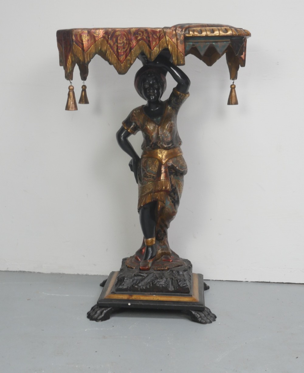 A 19th-century carved polychrome and gilded wooden Venetian side table depicting a figural stand supporting a draped canopy top with hanging tassels.