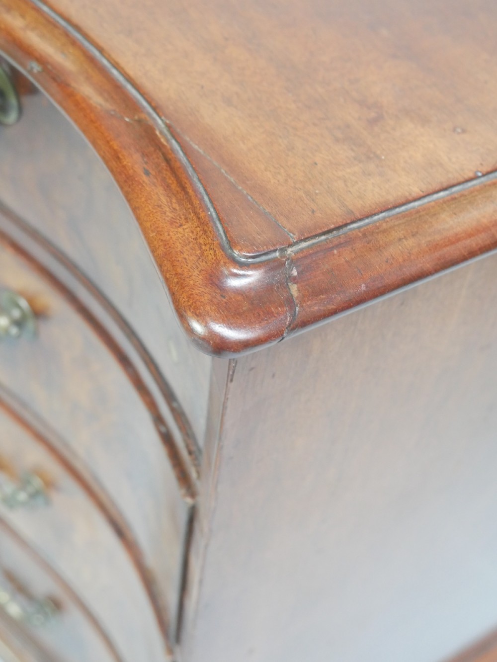 An eighteenth-century Georgian serpentine-fronted mahogany chest of drawers featuring brass swan-neck handles and bracket feet. View IV