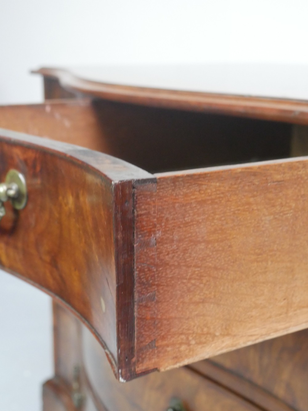 An eighteenth-century Georgian serpentine-fronted mahogany chest of drawers featuring brass swan-neck handles and bracket feet. View V