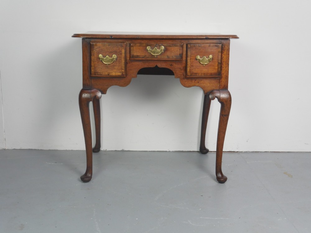 An eighteenth-century Georgian oak lowboy table featuring three drawers with brass handles, a shaped apron, and four cabriole legs ending in pad feet.