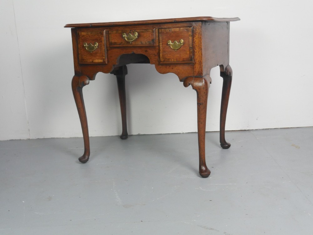 An eighteenth-century Georgian oak lowboy table featuring three drawers with brass handles, a shaped apron, and four cabriole legs ending in pad feet. View II