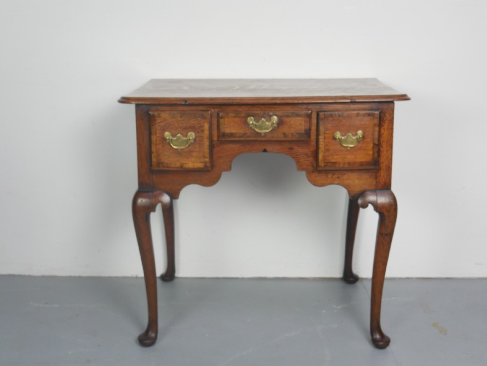 An eighteenth-century Georgian oak lowboy table featuring three drawers with brass handles, a shaped apron, and four cabriole legs ending in pad feet. View XIII