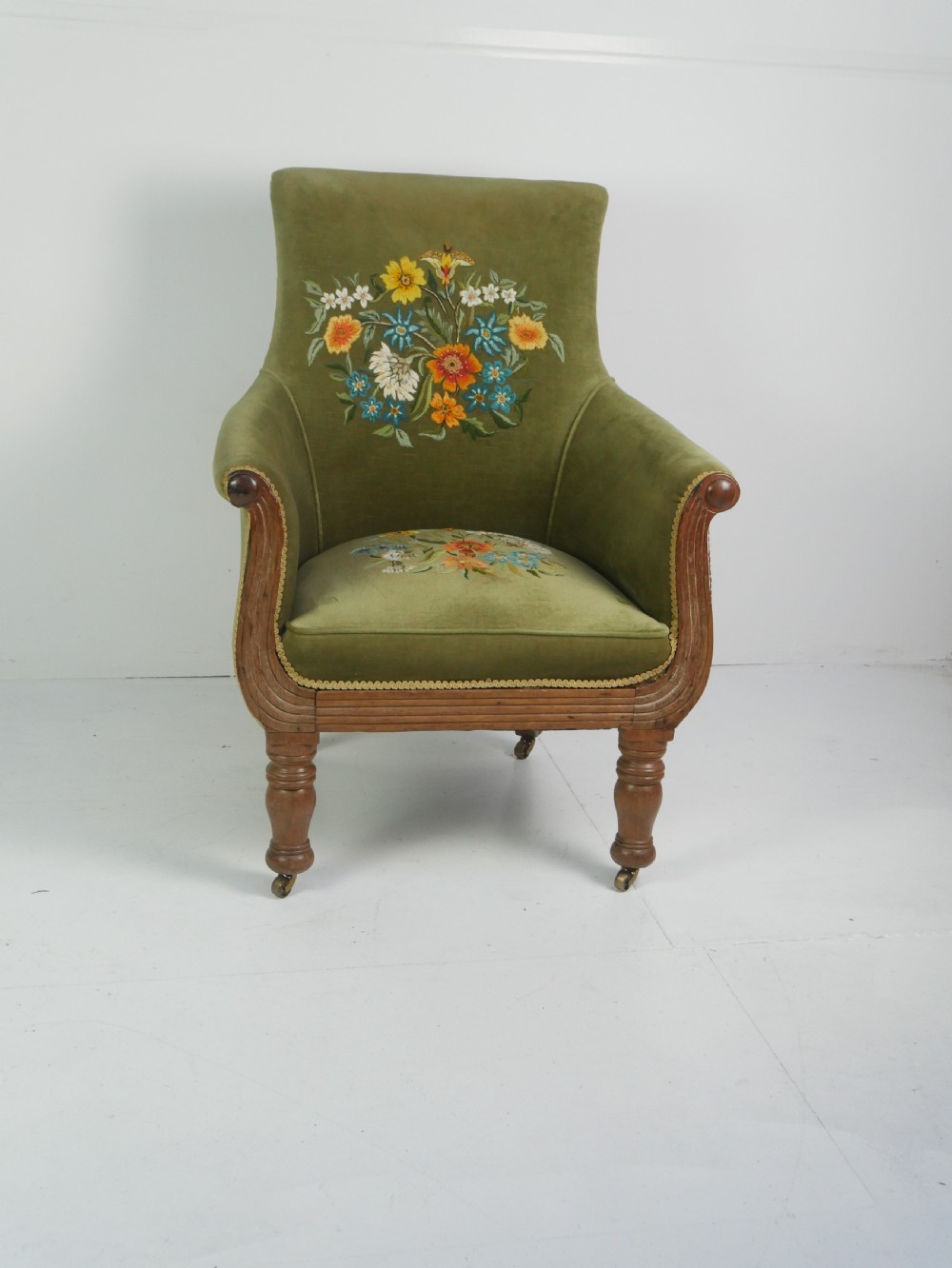 A Regency period style armchair upholstered in olive green velvet with floral needlepoint embroidery on the backrest and seat cushion.