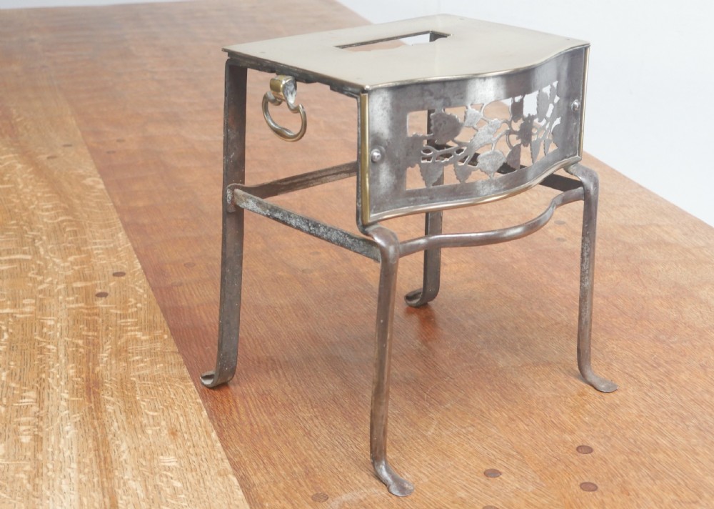 A small Georgian brass and steel footman featuring a top handle slot, side ring handles, and a pierced decorative front apron raised on shaped legs.