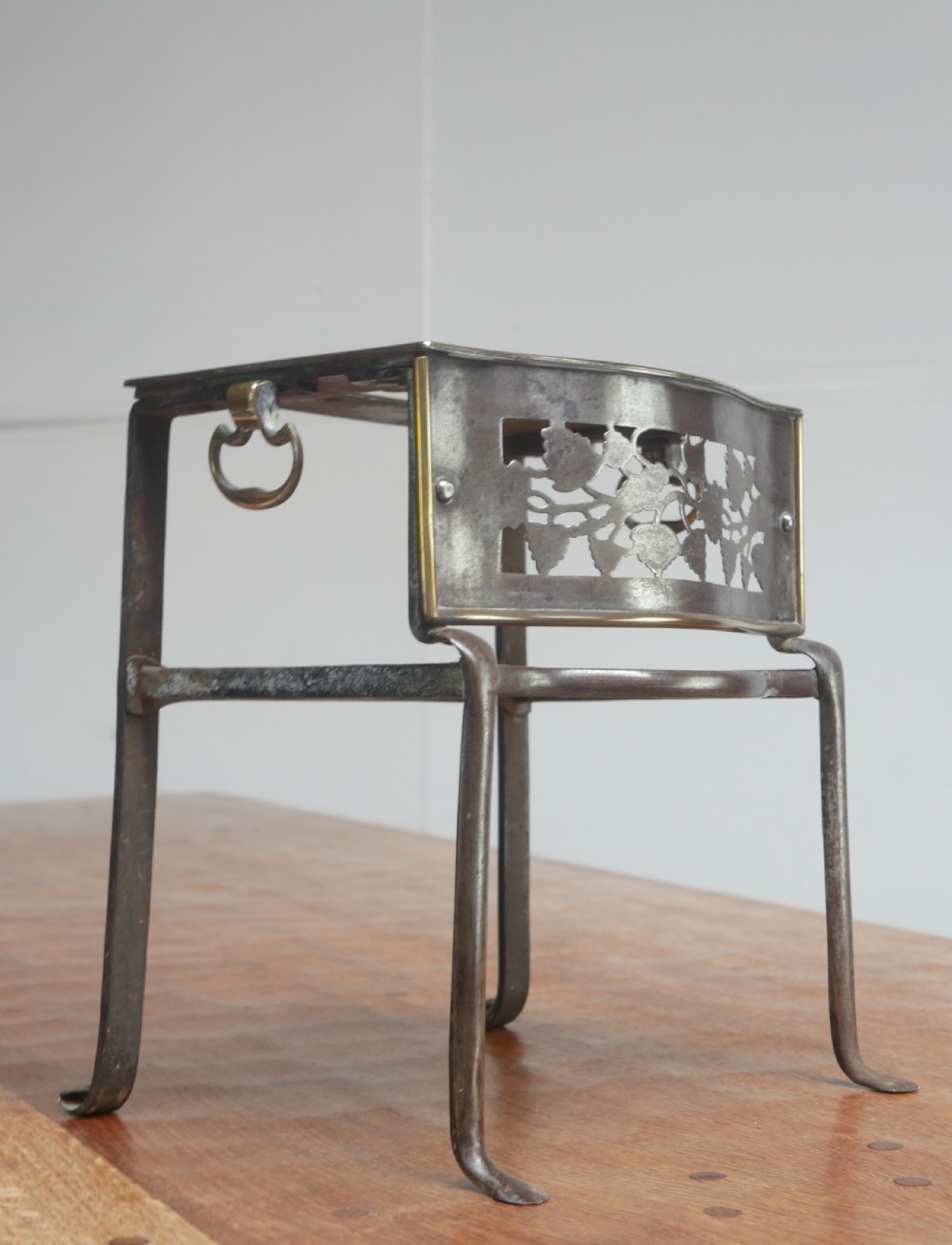 A small Georgian brass and steel footman featuring a top handle slot, side ring handles, and a pierced decorative front apron raised on shaped legs. View II