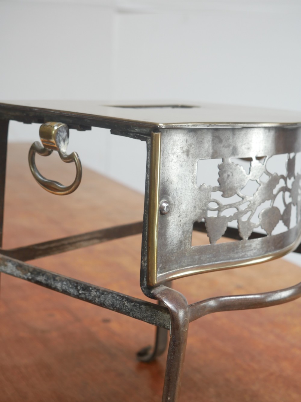 A small Georgian brass and steel footman featuring a top handle slot, side ring handles, and a pierced decorative front apron raised on shaped legs. View III