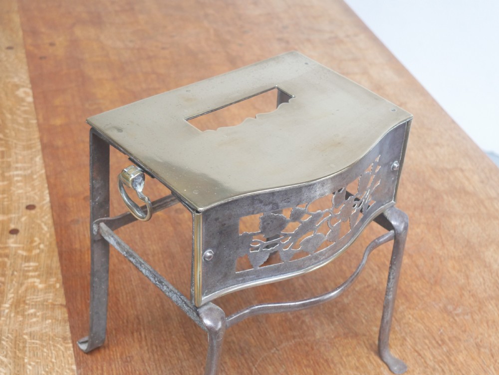 A small Georgian brass and steel footman featuring a top handle slot, side ring handles, and a pierced decorative front apron raised on shaped legs. View X