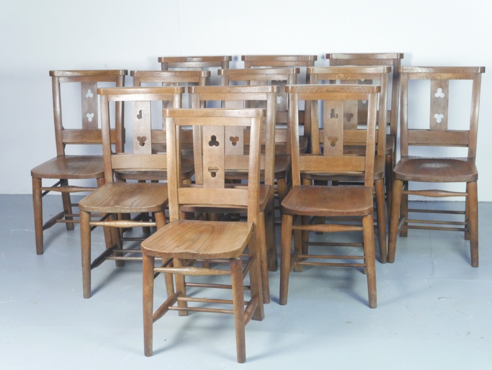 A set of twelve solid oak dining chairs featuring openwork back splats with trefoil cutouts and square legs supported by stretchers.