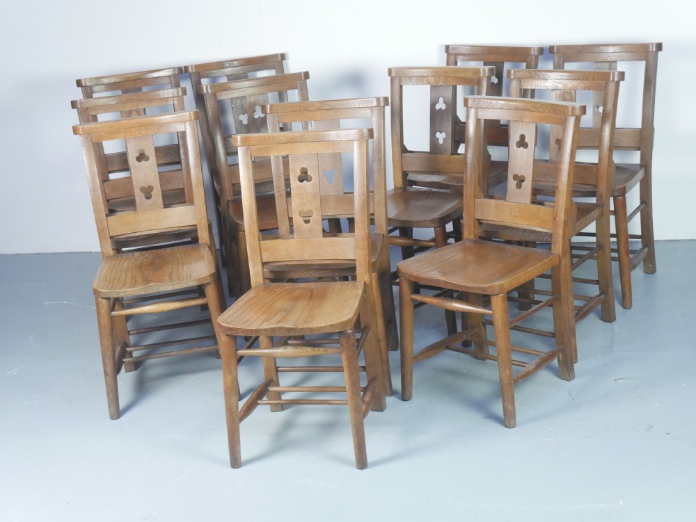 A set of twelve solid oak dining chairs featuring openwork back splats with trefoil cutouts and square legs supported by stretchers. View XIV