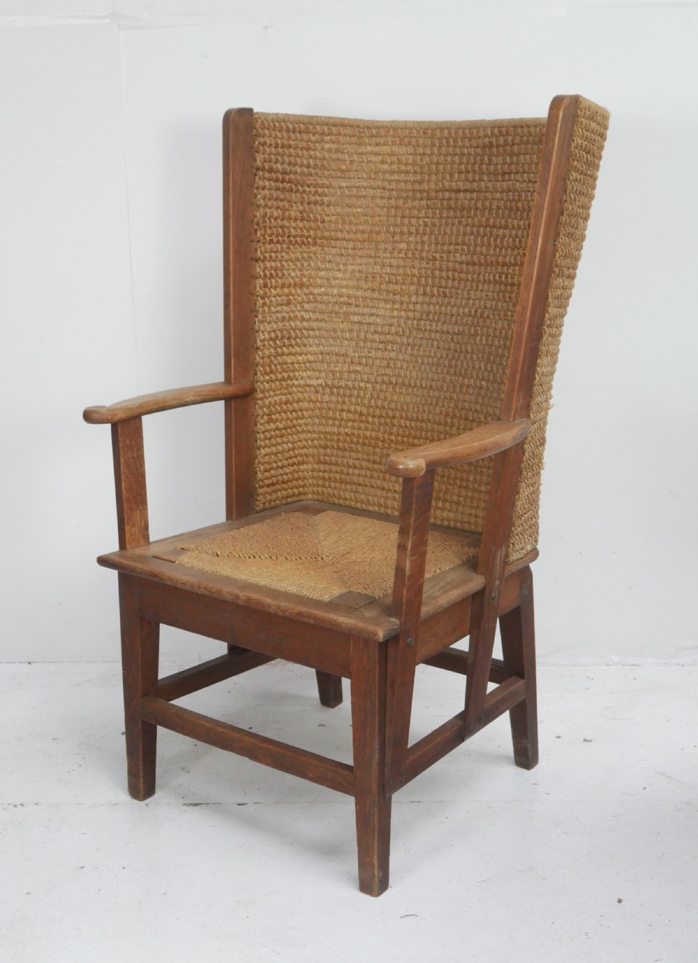 A traditional full-sized Scottish Orkney armchair featuring a timber oak frame, flat wooden armrests, a rush seat, and a tall hand-woven oat straw backrest. View X