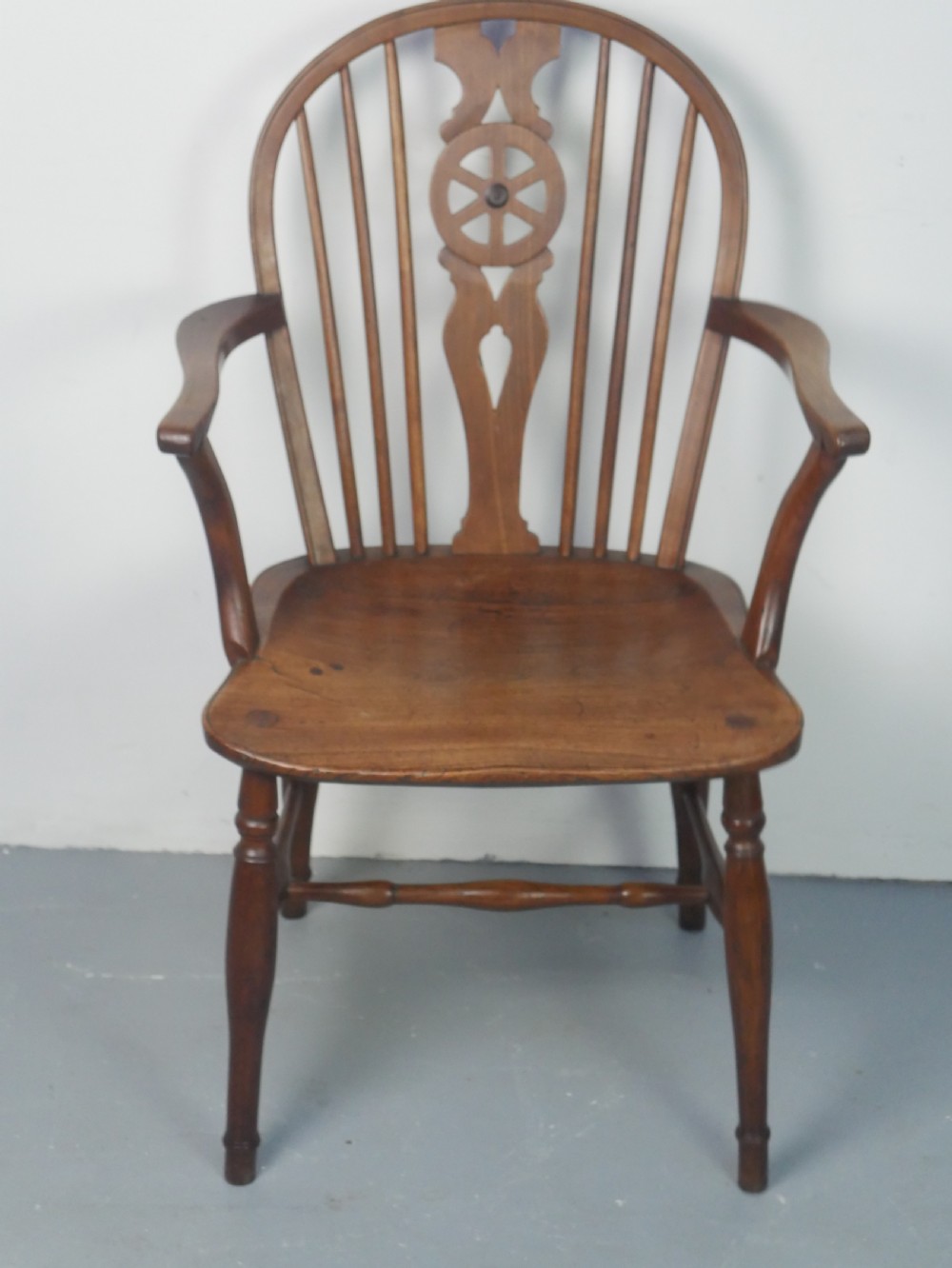 A Regency fruitwood Windsor armchair featuring a hoop back, a pierced wheelback central splat, turned spindles, shaped armrests, a carved saddle seat, and turned legs with stretchers.