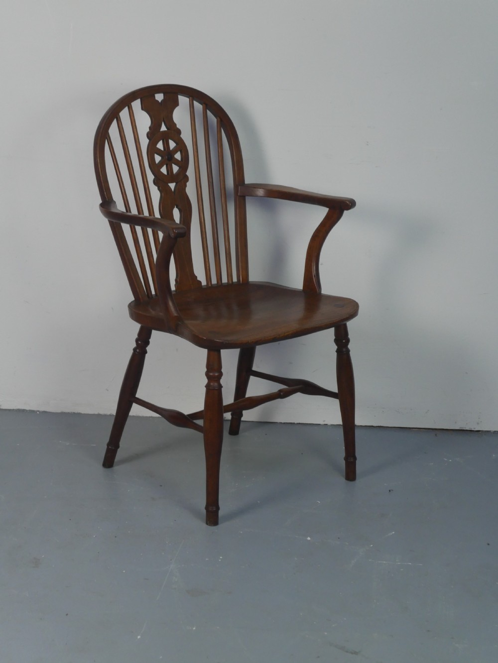A Regency fruitwood Windsor armchair featuring a hoop back, a pierced wheelback central splat, turned spindles, shaped armrests, a carved saddle seat, and turned legs with stretchers. View II