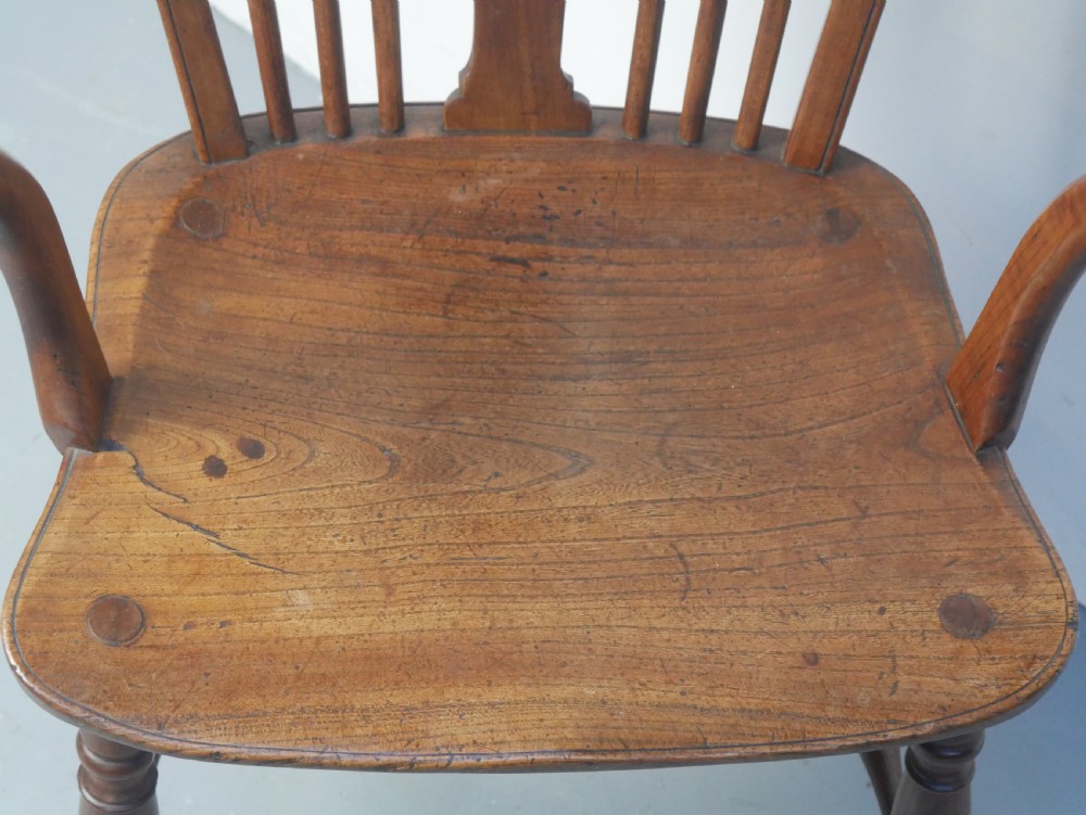 A Regency fruitwood Windsor armchair featuring a hoop back, a pierced wheelback central splat, turned spindles, shaped armrests, a carved saddle seat, and turned legs with stretchers. View III