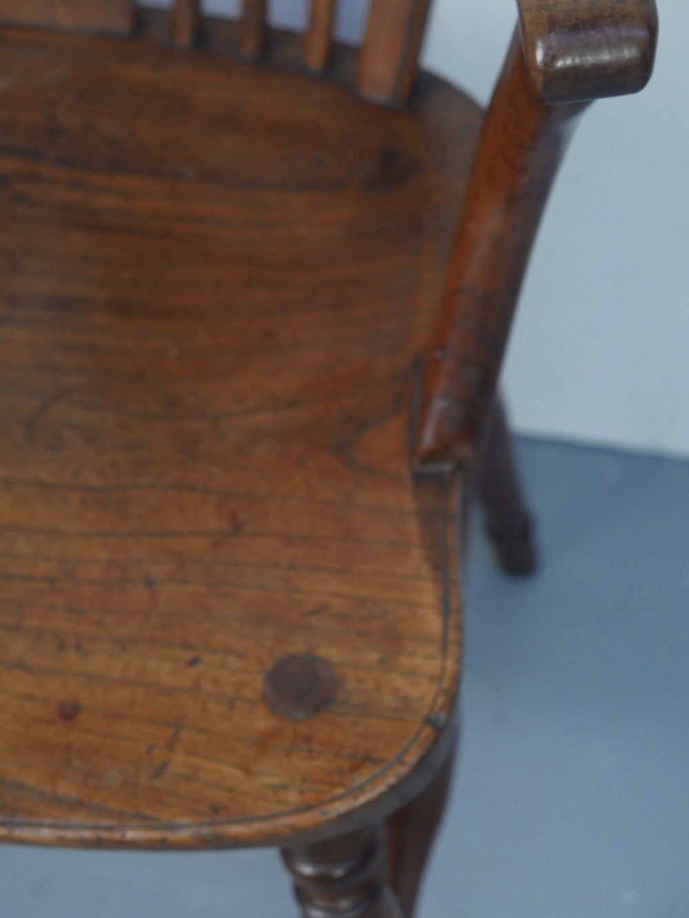 A Regency fruitwood Windsor armchair featuring a hoop back, a pierced wheelback central splat, turned spindles, shaped armrests, a carved saddle seat, and turned legs with stretchers. View IV