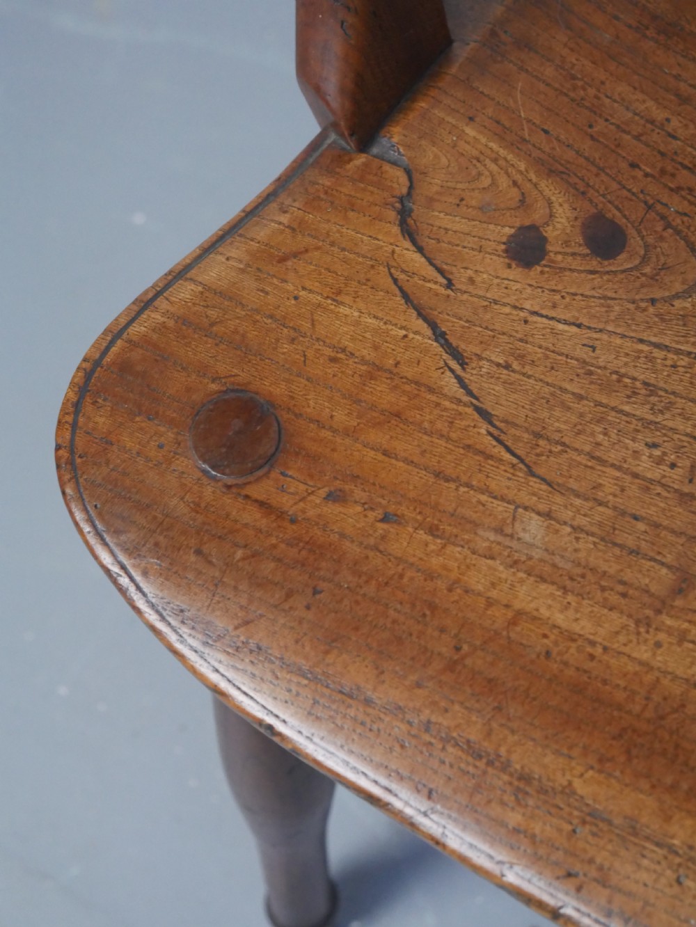 A Regency fruitwood Windsor armchair featuring a hoop back, a pierced wheelback central splat, turned spindles, shaped armrests, a carved saddle seat, and turned legs with stretchers. View V