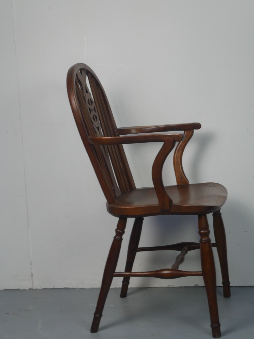 A Regency fruitwood Windsor armchair featuring a hoop back, a pierced wheelback central splat, turned spindles, shaped armrests, a carved saddle seat, and turned legs with stretchers. View VII