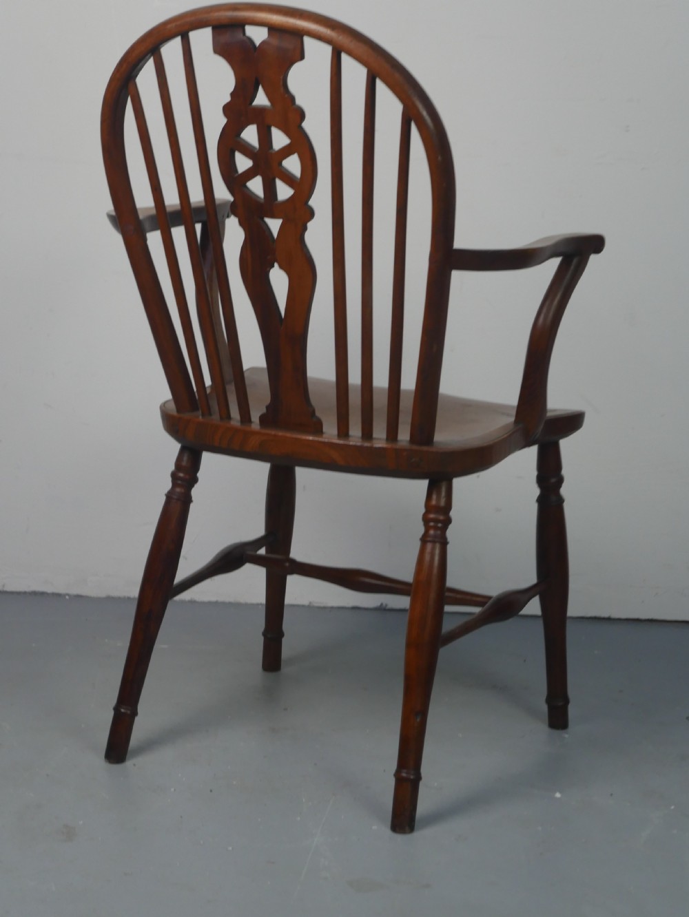 A Regency fruitwood Windsor armchair featuring a hoop back, a pierced wheelback central splat, turned spindles, shaped armrests, a carved saddle seat, and turned legs with stretchers. View VIII