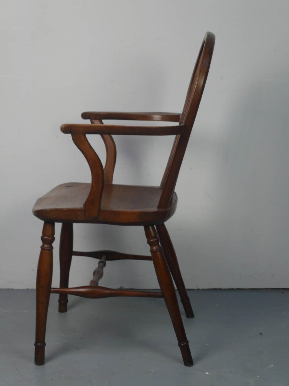 A Regency fruitwood Windsor armchair featuring a hoop back, a pierced wheelback central splat, turned spindles, shaped armrests, a carved saddle seat, and turned legs with stretchers. View IX