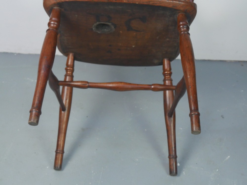 A Regency fruitwood Windsor armchair featuring a hoop back, a pierced wheelback central splat, turned spindles, shaped armrests, a carved saddle seat, and turned legs with stretchers. View X