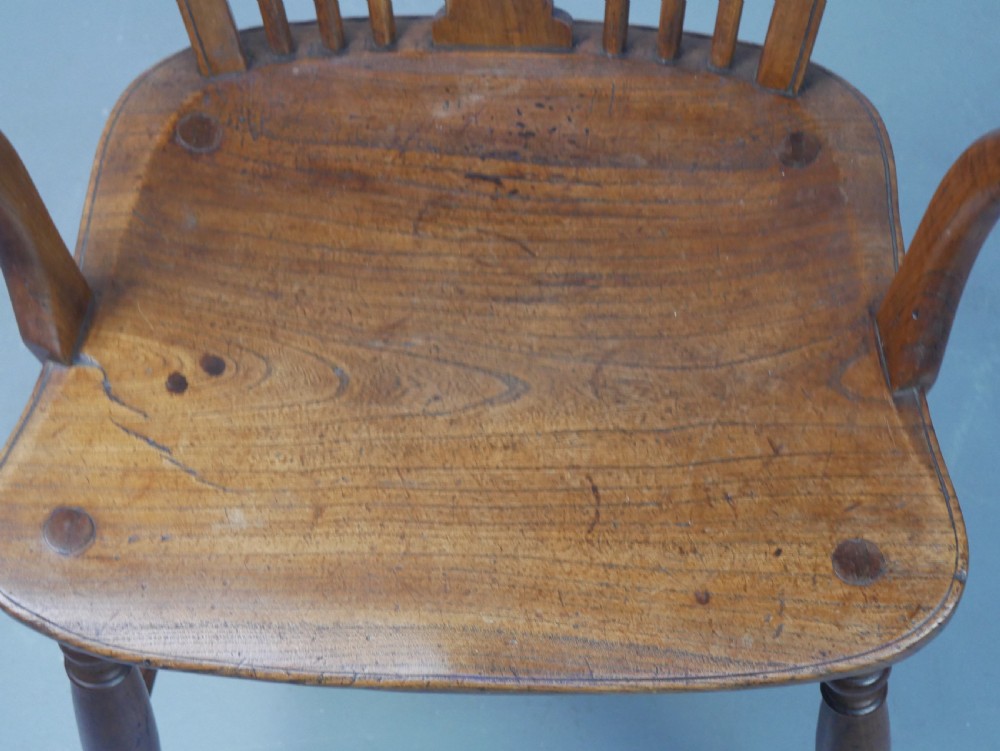 A Regency fruitwood Windsor armchair featuring a hoop back, a pierced wheelback central splat, turned spindles, shaped armrests, a carved saddle seat, and turned legs with stretchers. View XII