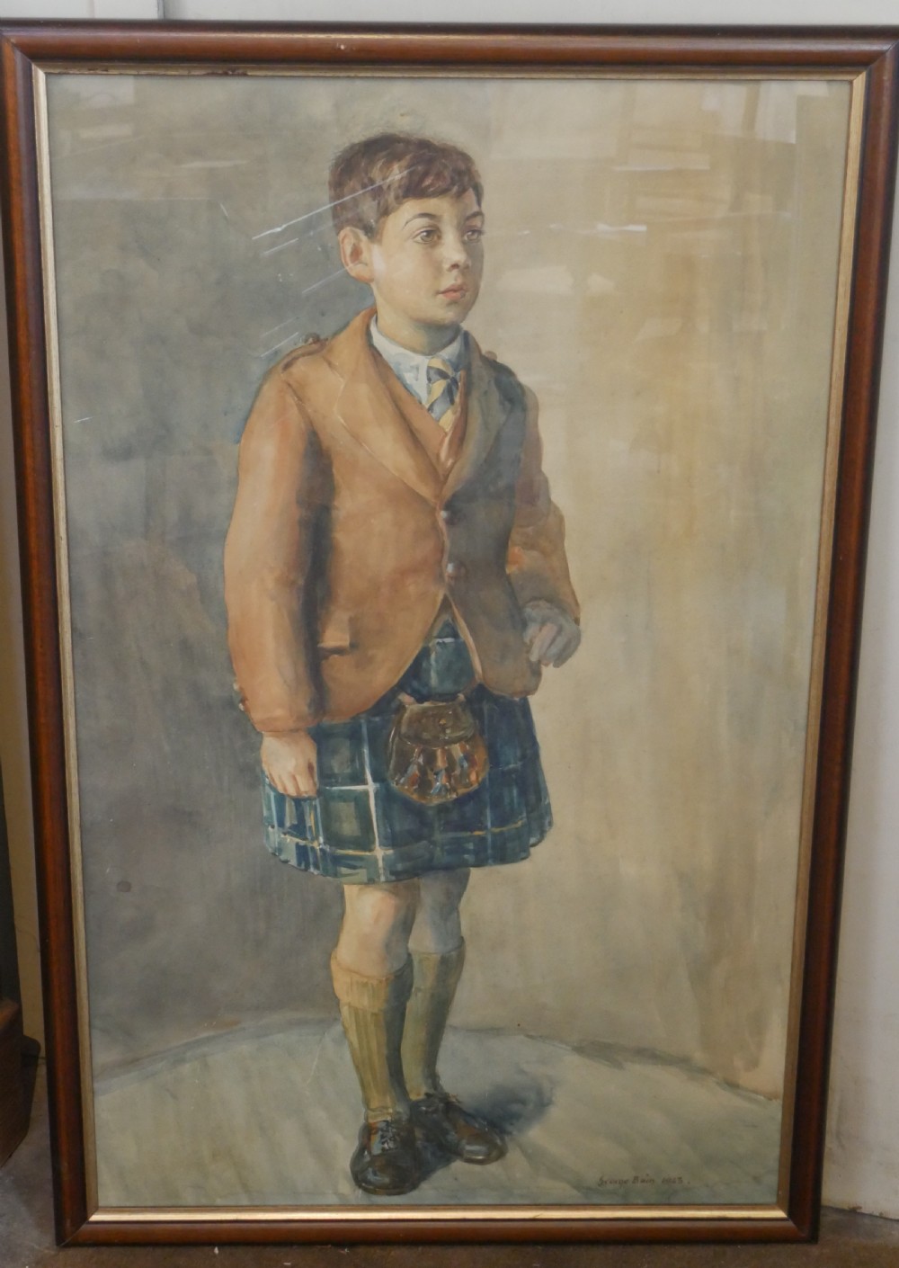 A framed watercolour portrait depicting a young boy standing in full Scottish Highland dress with a brown jacket and tartan kilt.