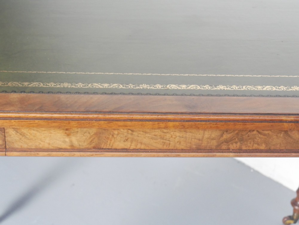 A light walnut writing table featuring a green leather inset top with gilt tooling, a single frieze drawer, and turned fluted legs on brass castors. View II