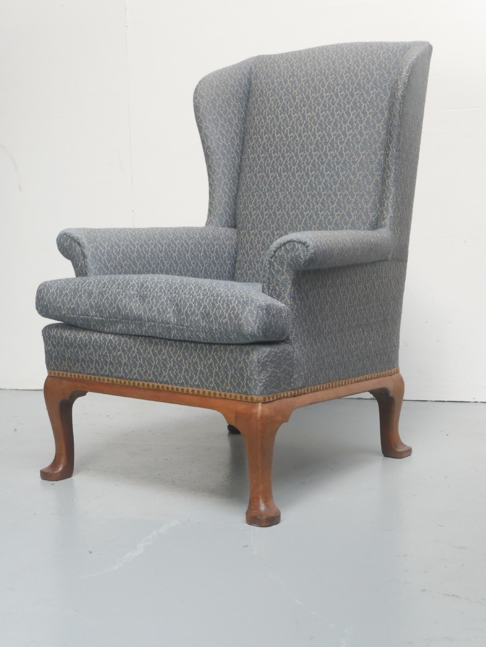 A high-backed wingback armchair upholstered in slate blue patterned fabric, featuring scrolled armrests and wooden cabriole legs.