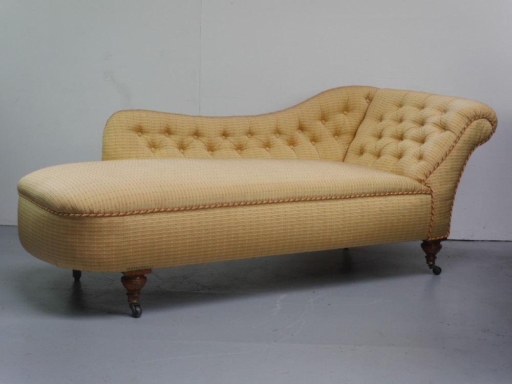A 19th-century Victorian chaise longue upholstered in a yellow patterned fabric with deep buttoning on the curved backrest and turned mahogany legs on brass castors.