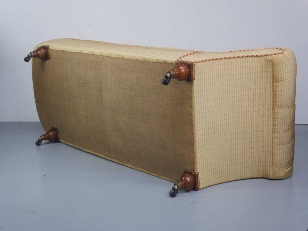 A 19th-century Victorian chaise longue upholstered in a yellow patterned fabric with deep buttoning on the curved backrest and turned mahogany legs on brass castors. View II