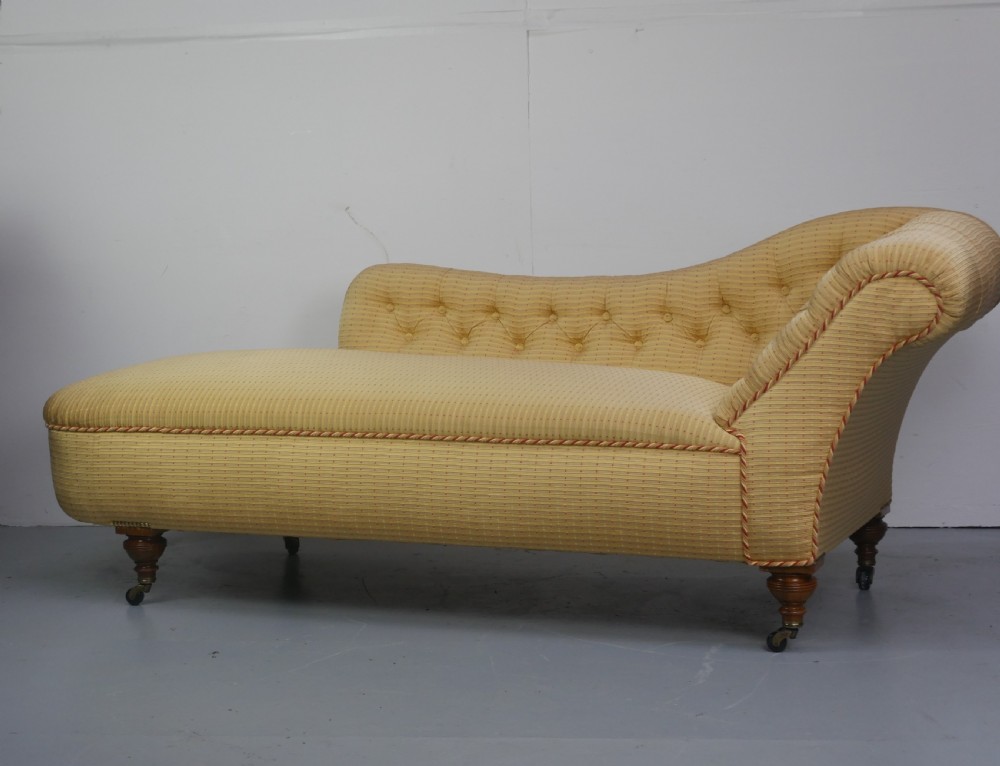 A 19th-century Victorian chaise longue upholstered in a yellow patterned fabric with deep buttoning on the curved backrest and turned mahogany legs on brass castors. View VI