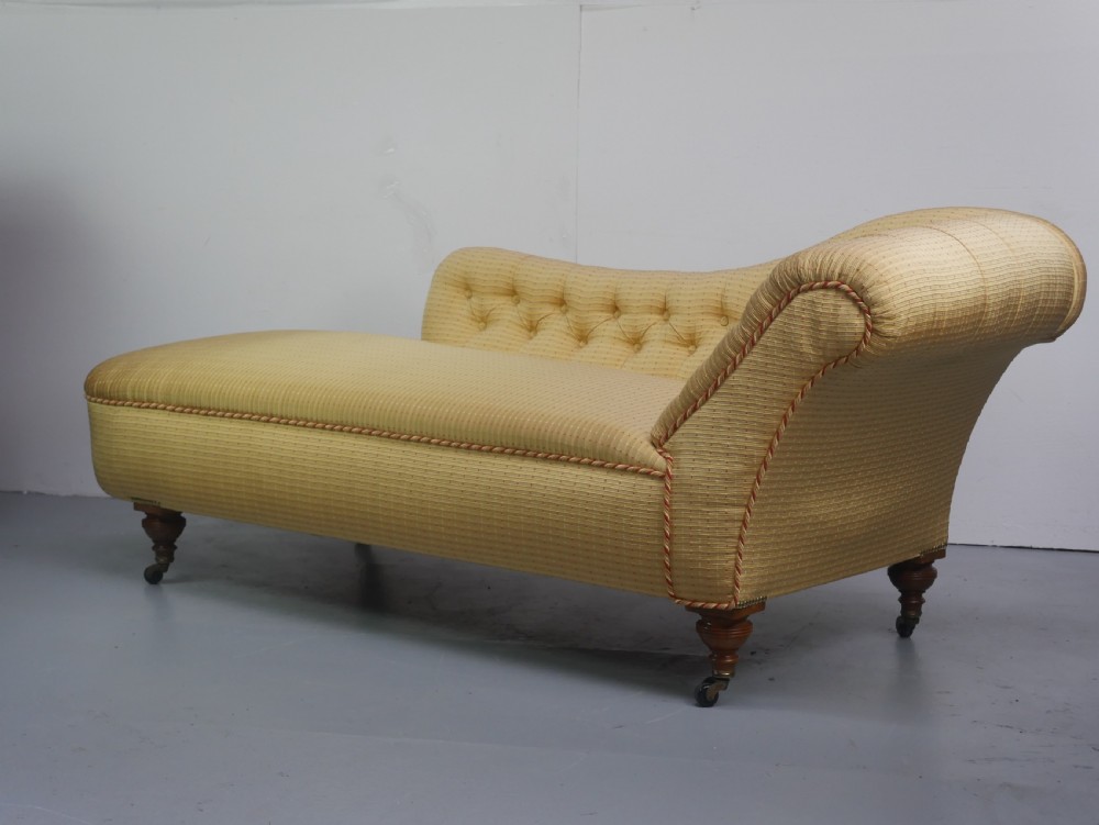 A 19th-century Victorian chaise longue upholstered in a yellow patterned fabric with deep buttoning on the curved backrest and turned mahogany legs on brass castors. View VII