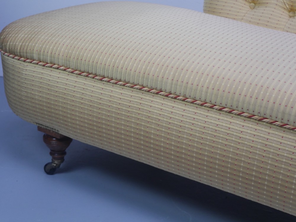 A 19th-century Victorian chaise longue upholstered in a yellow patterned fabric with deep buttoning on the curved backrest and turned mahogany legs on brass castors. View X